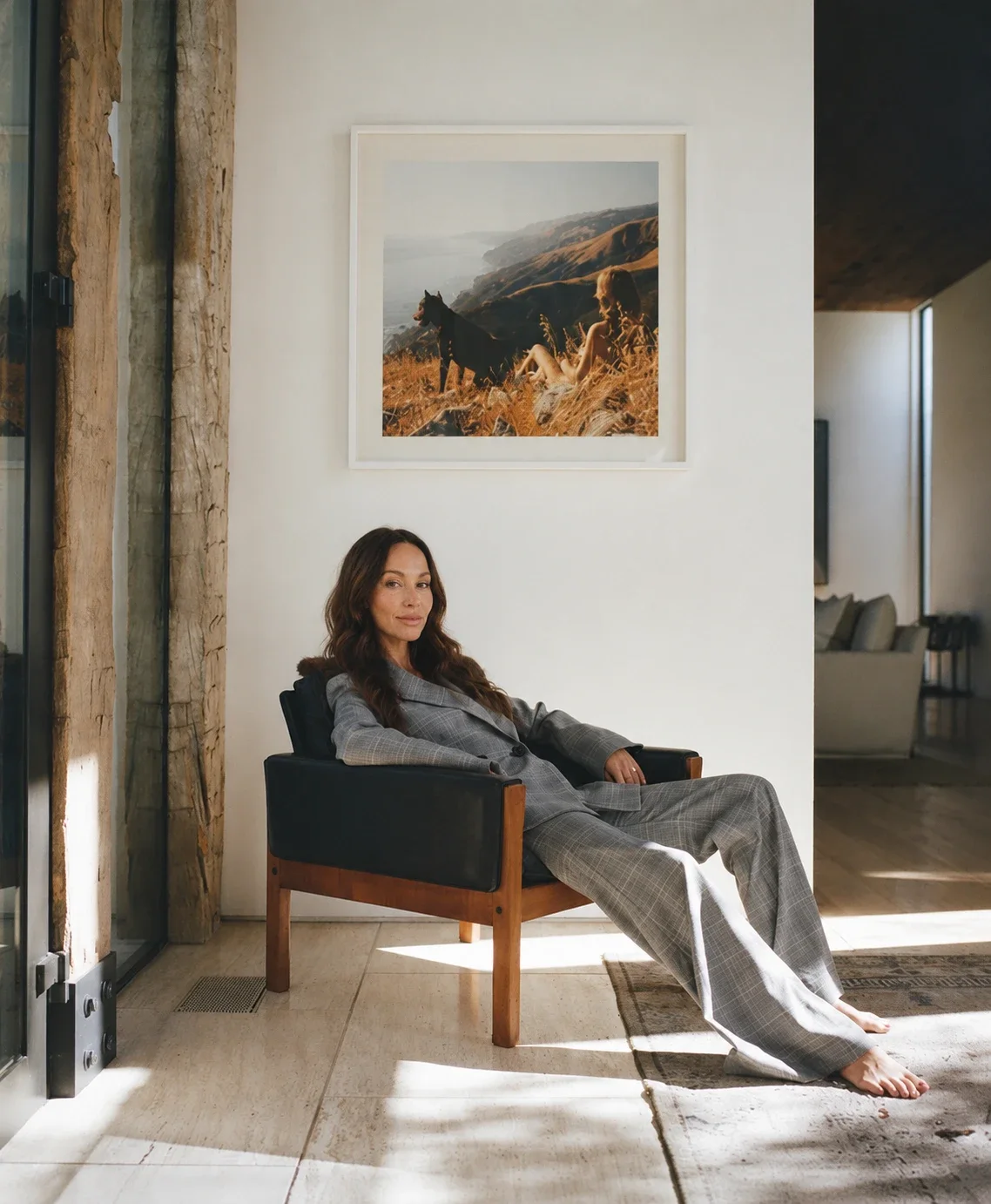 Rachel Urbach, founder of New Garde Labs, seated in a leather armchair in a sunlit room beneath a framed coastal photograph.